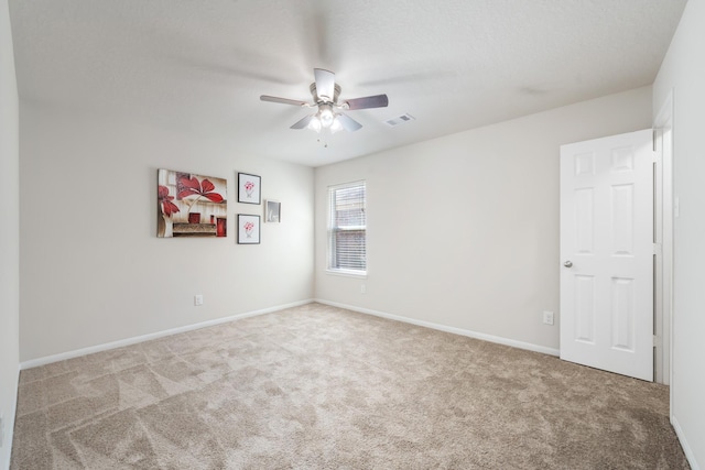 carpeted spare room with visible vents, a ceiling fan, and baseboards