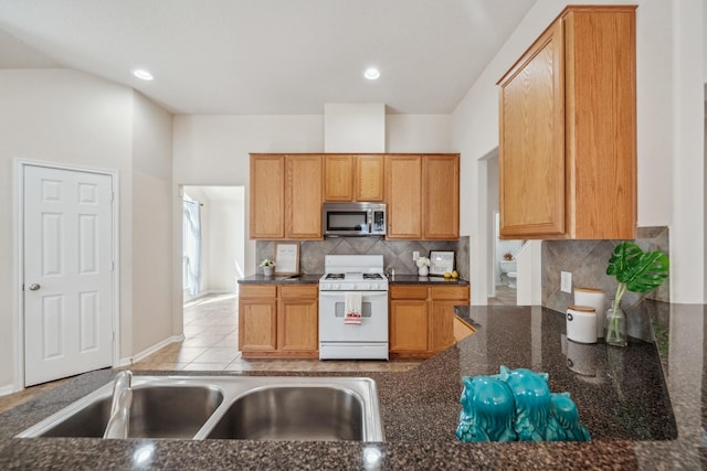 kitchen featuring dark stone countertops, backsplash, a sink, stainless steel microwave, and gas range gas stove