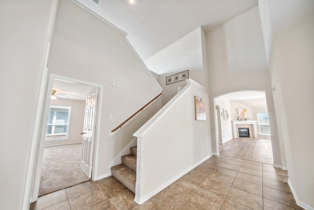 stairway featuring tile patterned floors, arched walkways, a glass covered fireplace, and high vaulted ceiling
