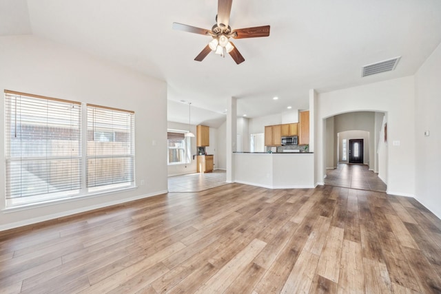 unfurnished living room with arched walkways, baseboards, visible vents, light wood-style floors, and ceiling fan