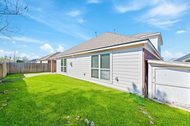 rear view of property with a lawn, a shingled roof, and fence
