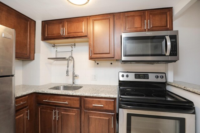 kitchen with light stone countertops, a sink, backsplash, and appliances with stainless steel finishes