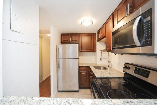 kitchen with light stone countertops, a sink, brown cabinets, and appliances with stainless steel finishes