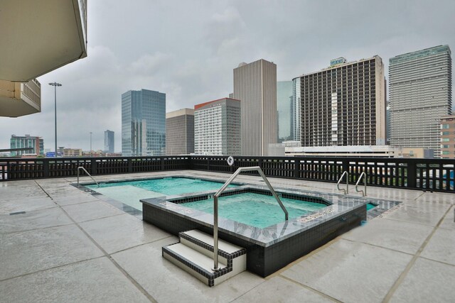 view of swimming pool with a patio area, a city view, and a community hot tub