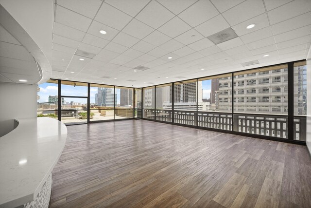 unfurnished room with expansive windows, a view of city, wood finished floors, and a drop ceiling