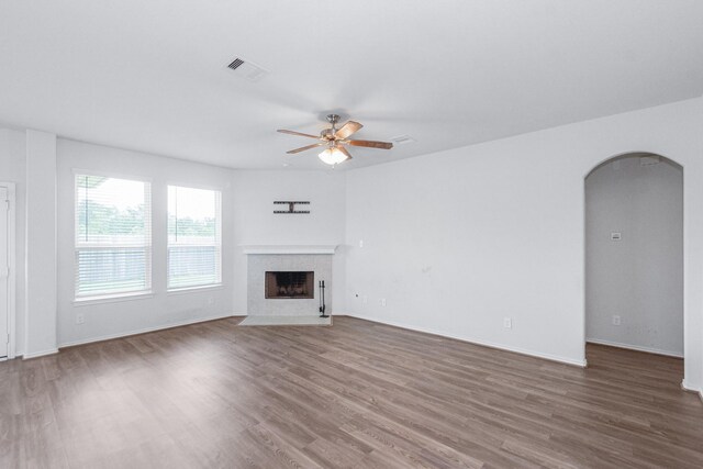 unfurnished living room with wood finished floors, ceiling fan, arched walkways, a tile fireplace, and visible vents