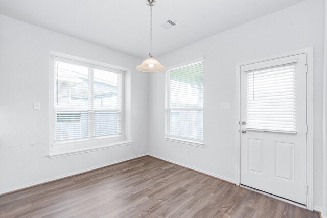unfurnished dining area with baseboards, wood finished floors, visible vents, and plenty of natural light