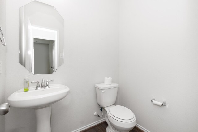 half bathroom featuring baseboards, wood finished floors, and toilet