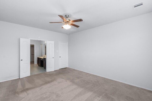 unfurnished bedroom featuring light carpet, visible vents, baseboards, a ceiling fan, and ensuite bath