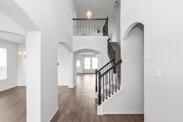 foyer featuring stairway, a high ceiling, an inviting chandelier, wood finished floors, and arched walkways