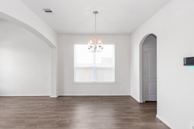 unfurnished dining area featuring an inviting chandelier, wood finished floors, visible vents, arched walkways, and baseboards