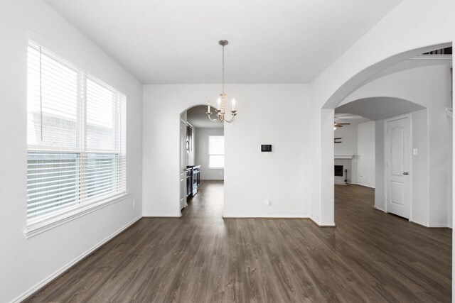 unfurnished dining area with arched walkways, baseboards, dark wood-type flooring, and an inviting chandelier