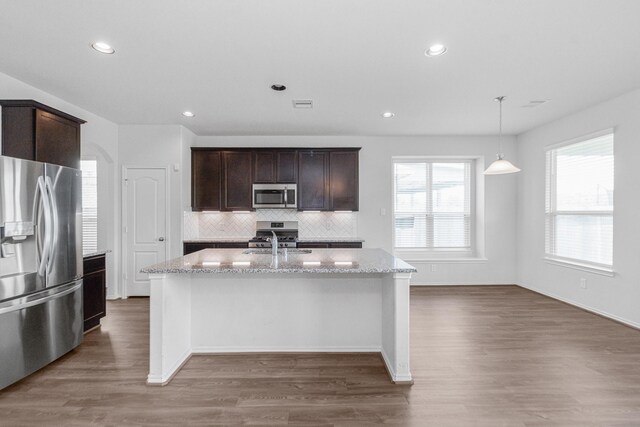 kitchen featuring light stone countertops, dark brown cabinets, appliances with stainless steel finishes, and a center island with sink
