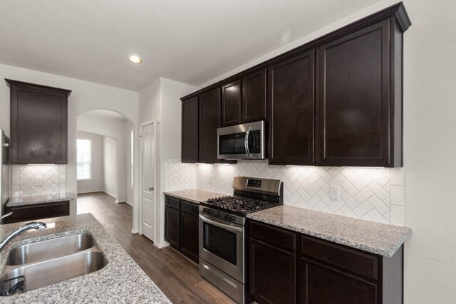 kitchen with stainless steel appliances, backsplash, a sink, arched walkways, and dark wood-type flooring
