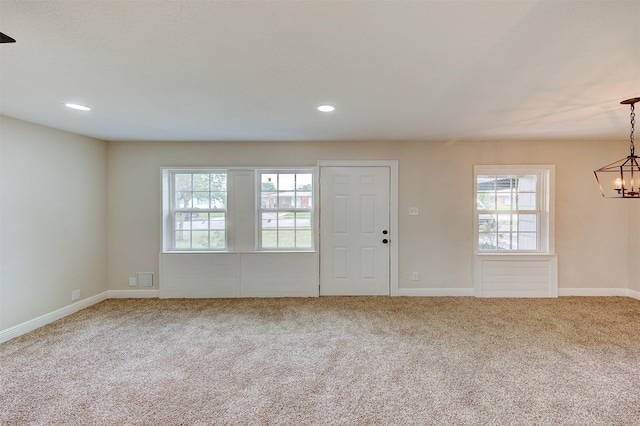 carpeted foyer entrance with baseboards, a healthy amount of sunlight, and an inviting chandelier