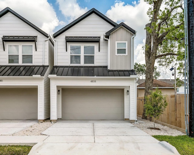 view of front facade featuring fence, an attached garage, a standing seam roof, driveway, and metal roof