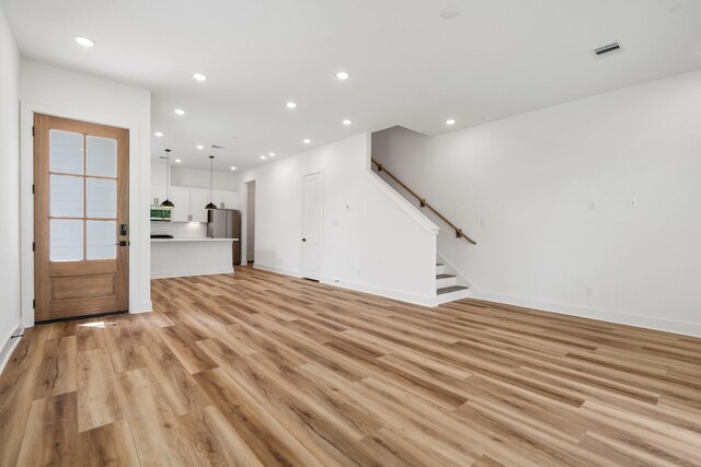 unfurnished living room featuring recessed lighting, light wood-type flooring, baseboards, and stairway
