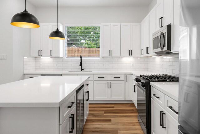 kitchen featuring light wood finished floors, stainless steel appliances, a sink, light countertops, and beverage cooler