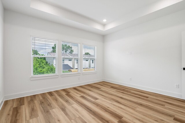 spare room featuring light wood-style flooring, baseboards, recessed lighting, and a raised ceiling