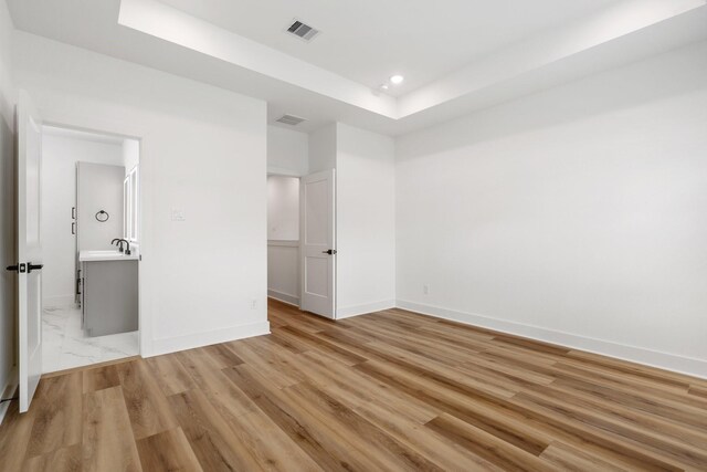 unfurnished bedroom with light wood finished floors, a tray ceiling, baseboards, visible vents, and recessed lighting