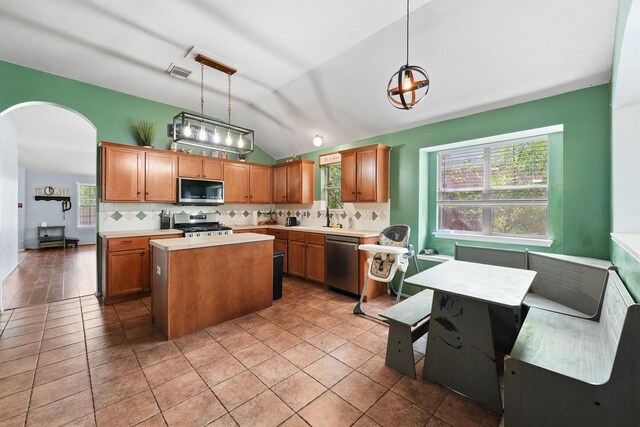 kitchen with appliances with stainless steel finishes, arched walkways, a center island, backsplash, and vaulted ceiling