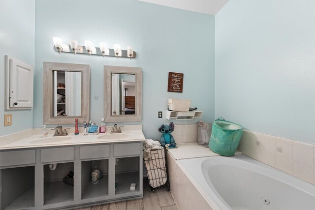 full bath featuring double vanity, a whirlpool tub, a sink, and wood finished floors