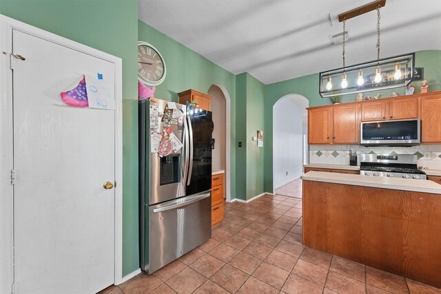 kitchen featuring light countertops, arched walkways, stainless steel appliances, decorative backsplash, and light tile patterned floors