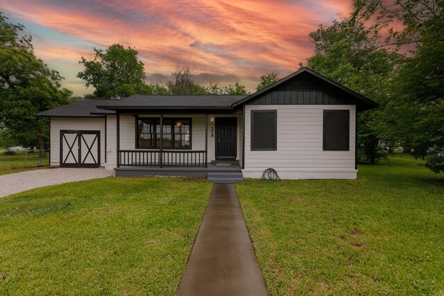 208 W Jefferson St, Trinity, TX 75862 - view of front of property with covered porch, an attached garage, a front yard, gravel driveway, and board and batten siding