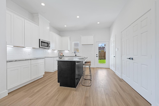 6726 Dumble St, Houston, TX 77021 - kitchen with stainless steel microwave, light wood finished floors, decorative backsplash, recessed lighting, and white cabinets