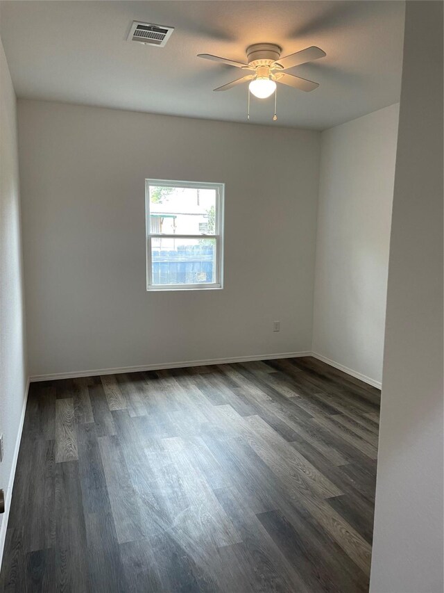empty room featuring ceiling fan, visible vents, baseboards, and dark wood-style flooring