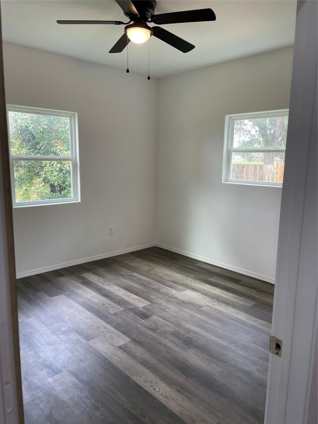 unfurnished room with dark wood finished floors, a ceiling fan, and baseboards