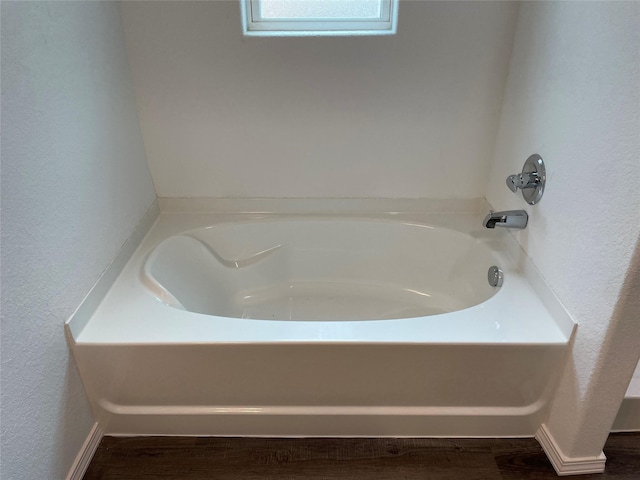 bathroom with a textured wall, baseboards, wood finished floors, and a tub