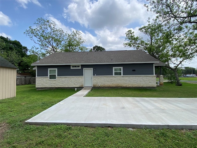 rear view of house featuring a yard, roof with shingles, stone siding, and a patio