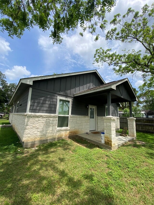 exterior space with stone siding, fence, board and batten siding, a yard, and a patio