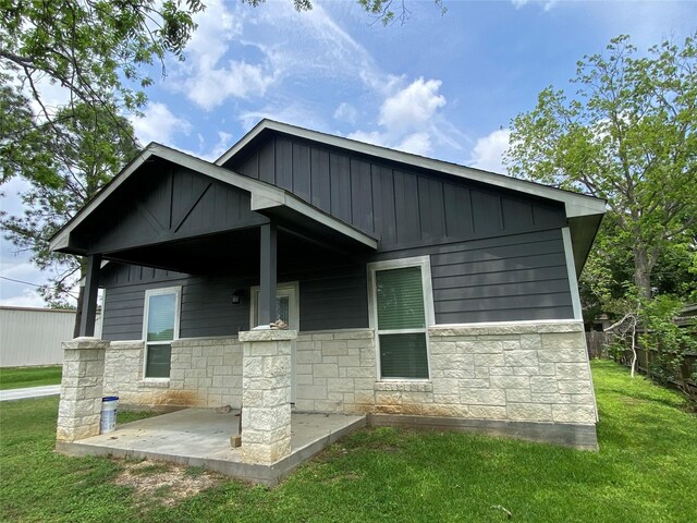 exterior space with board and batten siding, a yard, stone siding, and a patio