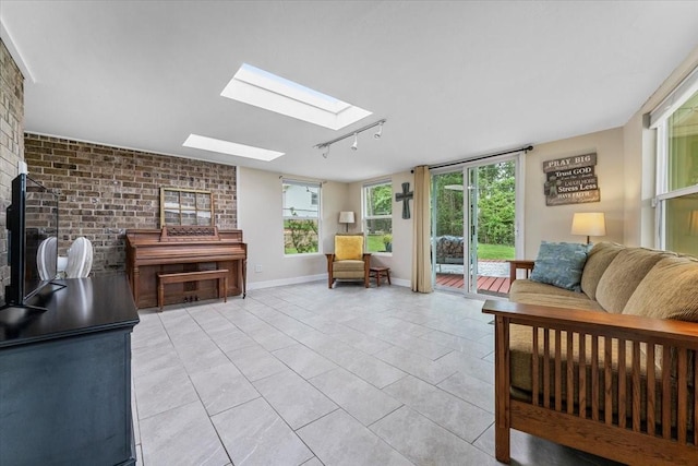 living area featuring light tile patterned flooring, track lighting, brick wall, baseboards, and a skylight