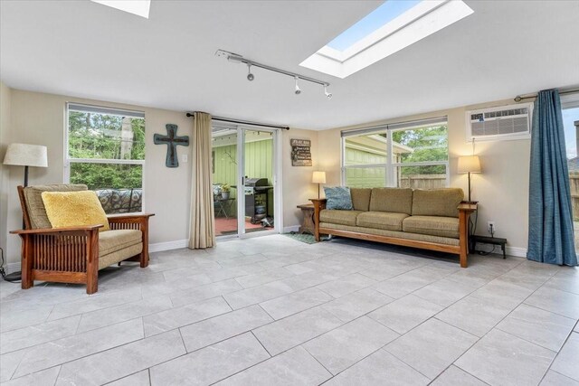 living area featuring a wall unit AC, a skylight, light tile patterned floors, track lighting, and baseboards