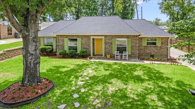 ranch-style home with brick siding, a front lawn, roof with shingles, and fence