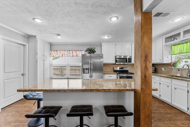 kitchen with a sink, a kitchen breakfast bar, stainless steel appliances, white cabinetry, and visible vents