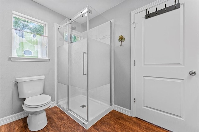 bathroom featuring baseboards, wood finished floors, toilet, and a shower stall