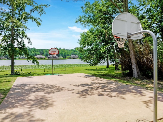 view of basketball court featuring a water view, a yard, and basketball hoop