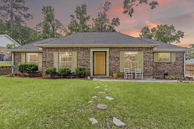 ranch-style home with a shingled roof, a yard, and brick siding