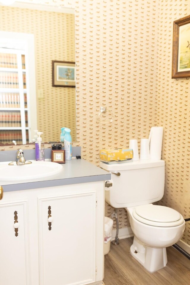 bathroom with wallpapered walls, wood finished floors, vanity, and toilet