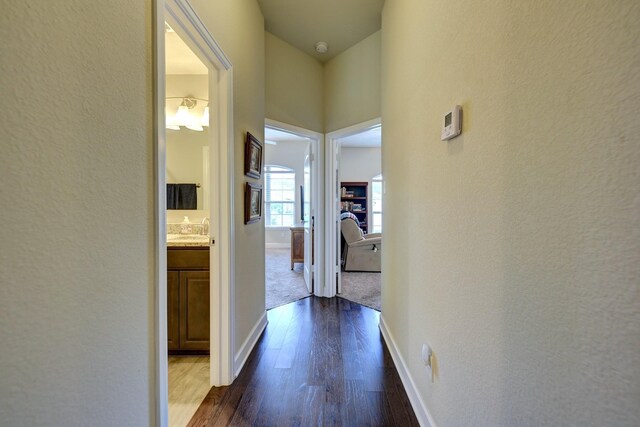 hall with a textured wall, baseboards, a sink, and dark wood-style flooring