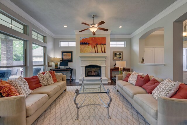 living room featuring a fireplace with raised hearth, a wealth of natural light, crown molding, and ceiling fan