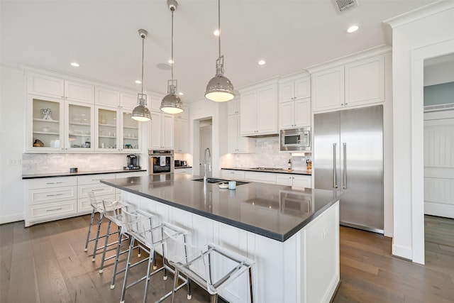 kitchen featuring built in appliances, dark countertops, a sink, and white cabinets