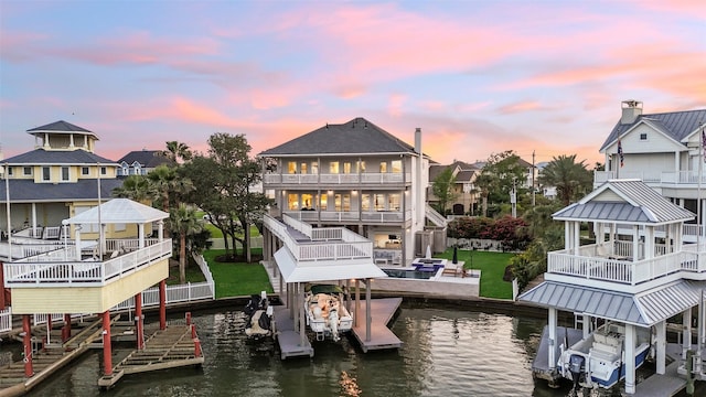 back of house at dusk featuring a water view, a balcony, boat lift, and a residential view