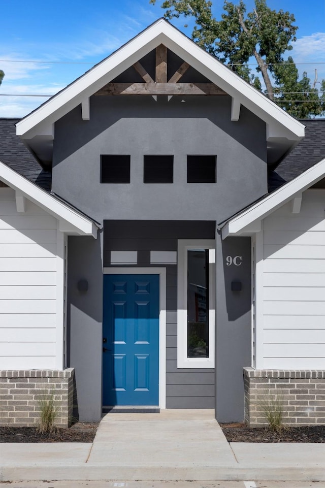 entrance to property with stucco siding and roof with shingles