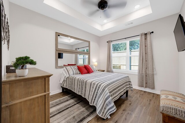 bedroom featuring recessed lighting, a tray ceiling, wood finished floors, visible vents, and baseboards