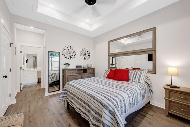 bedroom with a raised ceiling, wood finished floors, baseboards, and ensuite bathroom